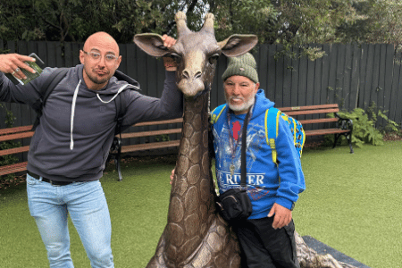 Disabled man standing with support worker next to cast iron giraffe statue