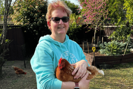 NDIS participant standing in backyard smiling at camera and holding a chicken