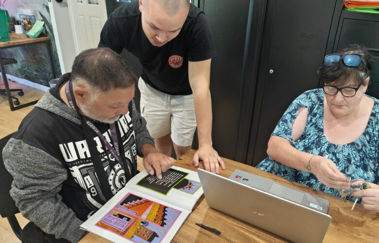 Two NDIS participants reading and using laptop at table
