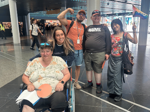 Group of NDIS participants and support workers at shopping mall, smiling at camera