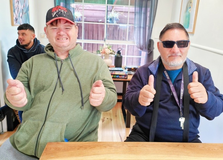 Two NDIS participants smiling and giving thumbs up to camera