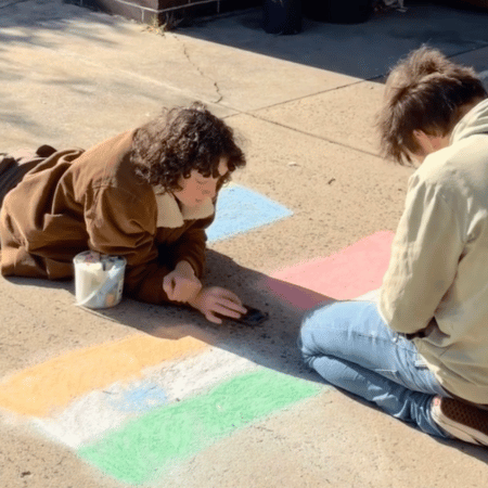 A man and woman drawing on concrete outside with chalk