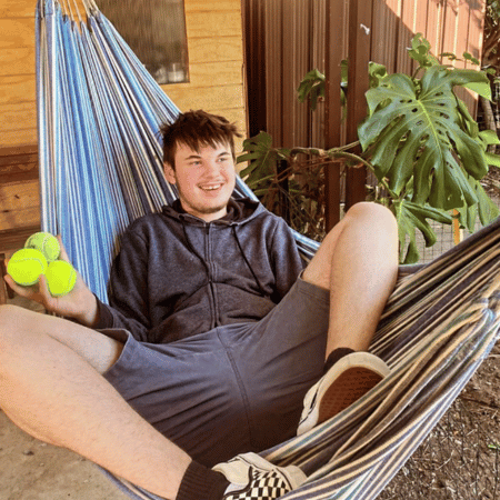 A man holding tennis balls and sitting in a hammock